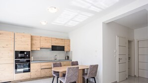 A modern kitchen with wooden cabinets, a built-in microwave, and a dining area with a table and chairs. - Sunny Pool by Interhome (Trogir/Okrug Gornji)