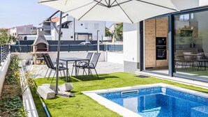 A modern outdoor patio with a pool, a barbecue grill, and a seating area with a table and chairs. - Sunny Pool by Interhome (Trogir/Okrug Gornji)