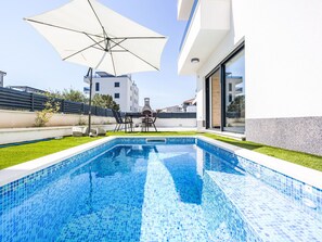 A swimming pool with a tiled edge, a patio area with a table and chairs, and a large umbrella. - Sunny Pool by Interhome (Trogir/Okrug Gornji)
