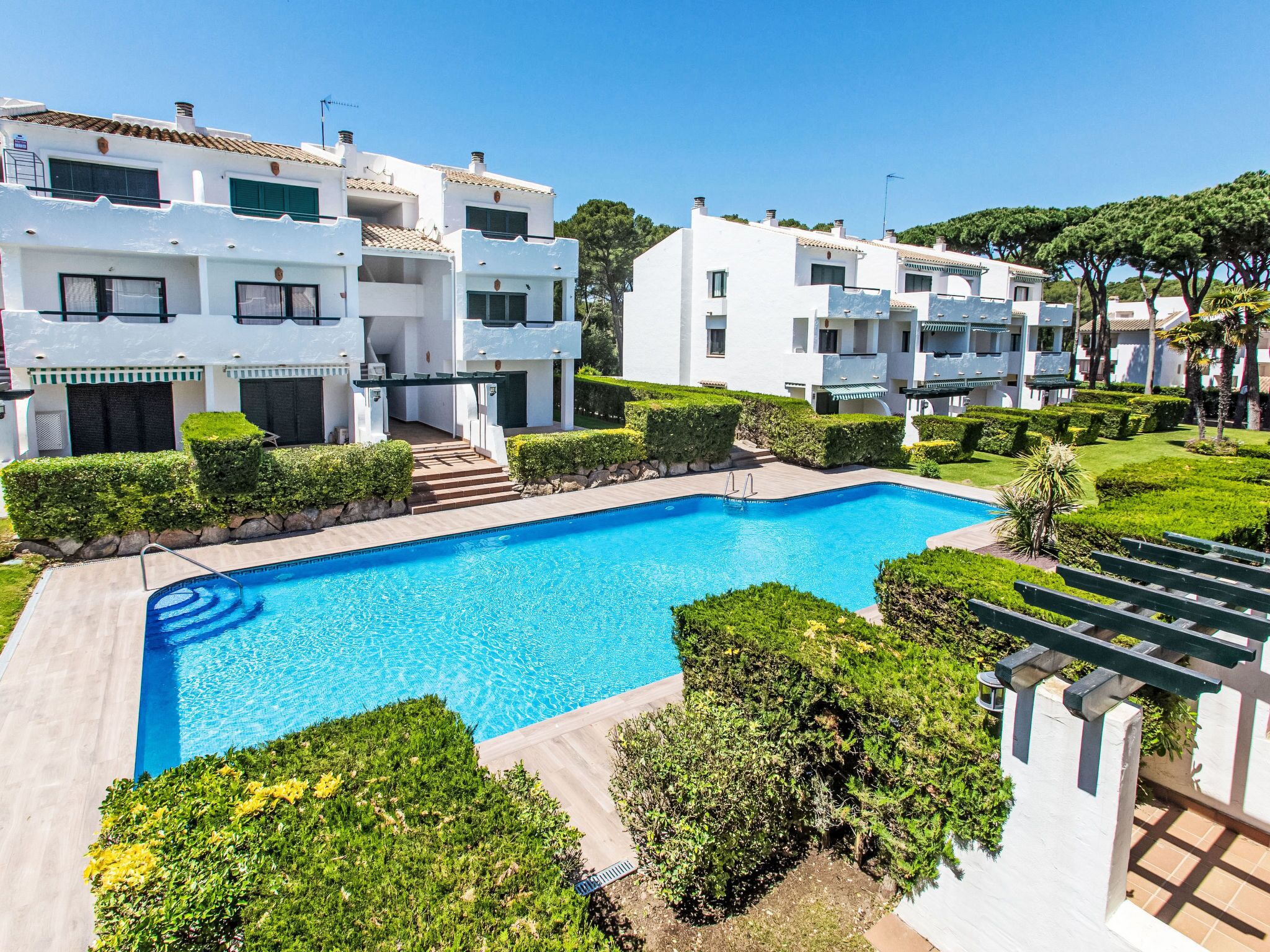 Un edificio residencial moderno con piscina, rodeado de abundante vegetación y un cielo azul despejado.