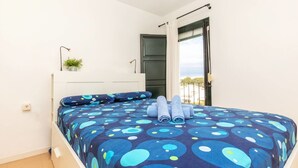 Ein Schlafzimmer mit einem Bett, einem Deckenventilator, einem Fenster mit Vorhängen und einer kleinen Pflanze auf dem Nachttisch.