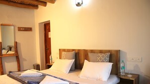 A neatly made bed with a blue and white patterned blanket, a wooden headboard, and two bedside tables with a bottle of water and a glass on one. - Karma Lodge (Leh)