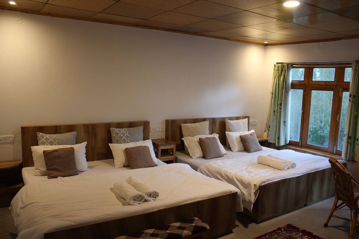 Habitación de hotel con dos camas, cabeceros de madera y un ventanal grande con cortinas.