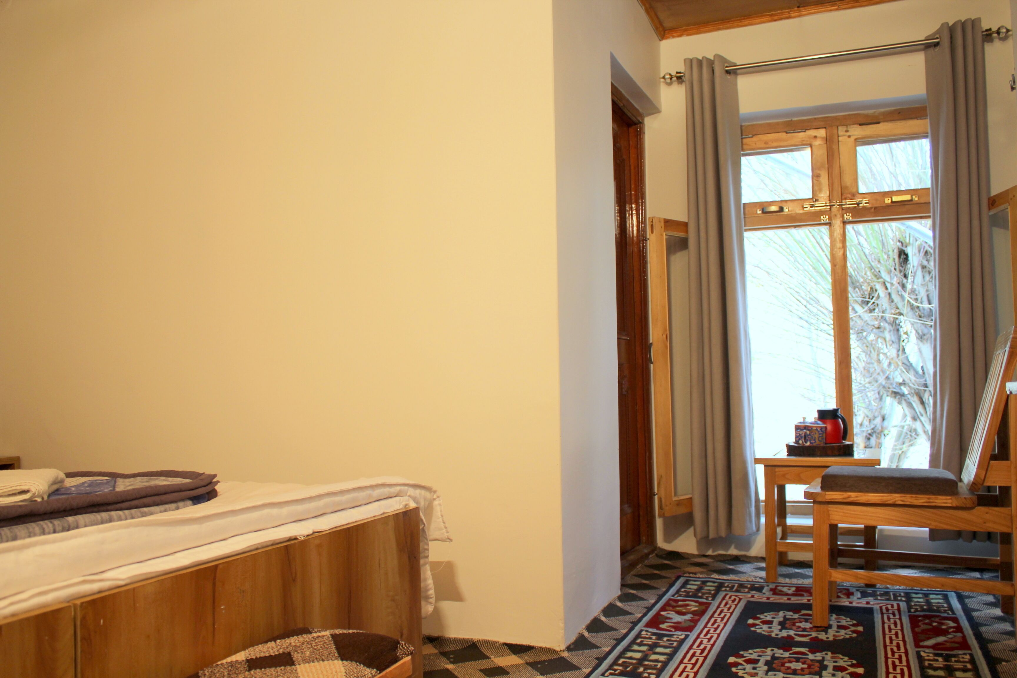 A bedroom with a bed, a chair, a window with curtains, and a patterned rug.