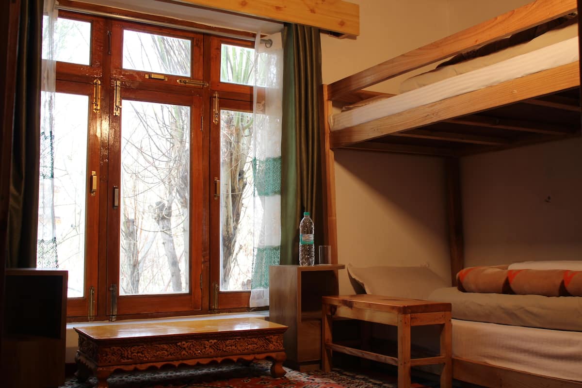 Una habitación con una cama de madera, una mesita pequeña y una ventana con cortinas.