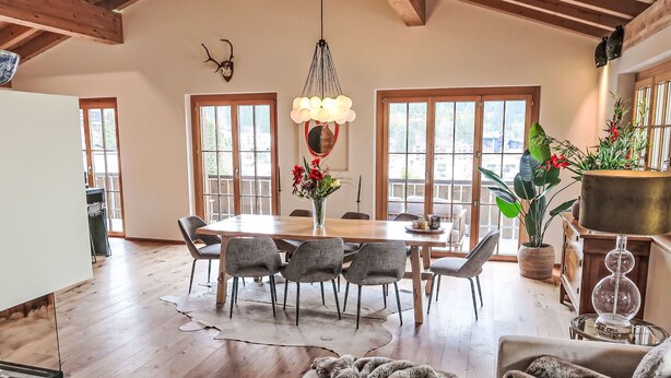 Een ruime eethoek met een houten tafel en stoelen, grote ramen en een kroonluchter.