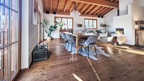 Een ruime woonkamer met een houten plafond, een eettafel met stoelen, een bank en een open haard.