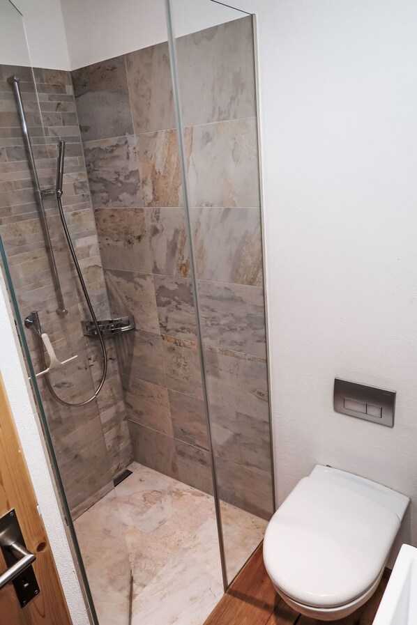 A shower with a glass door, a toilet, and a light switch on the wall.