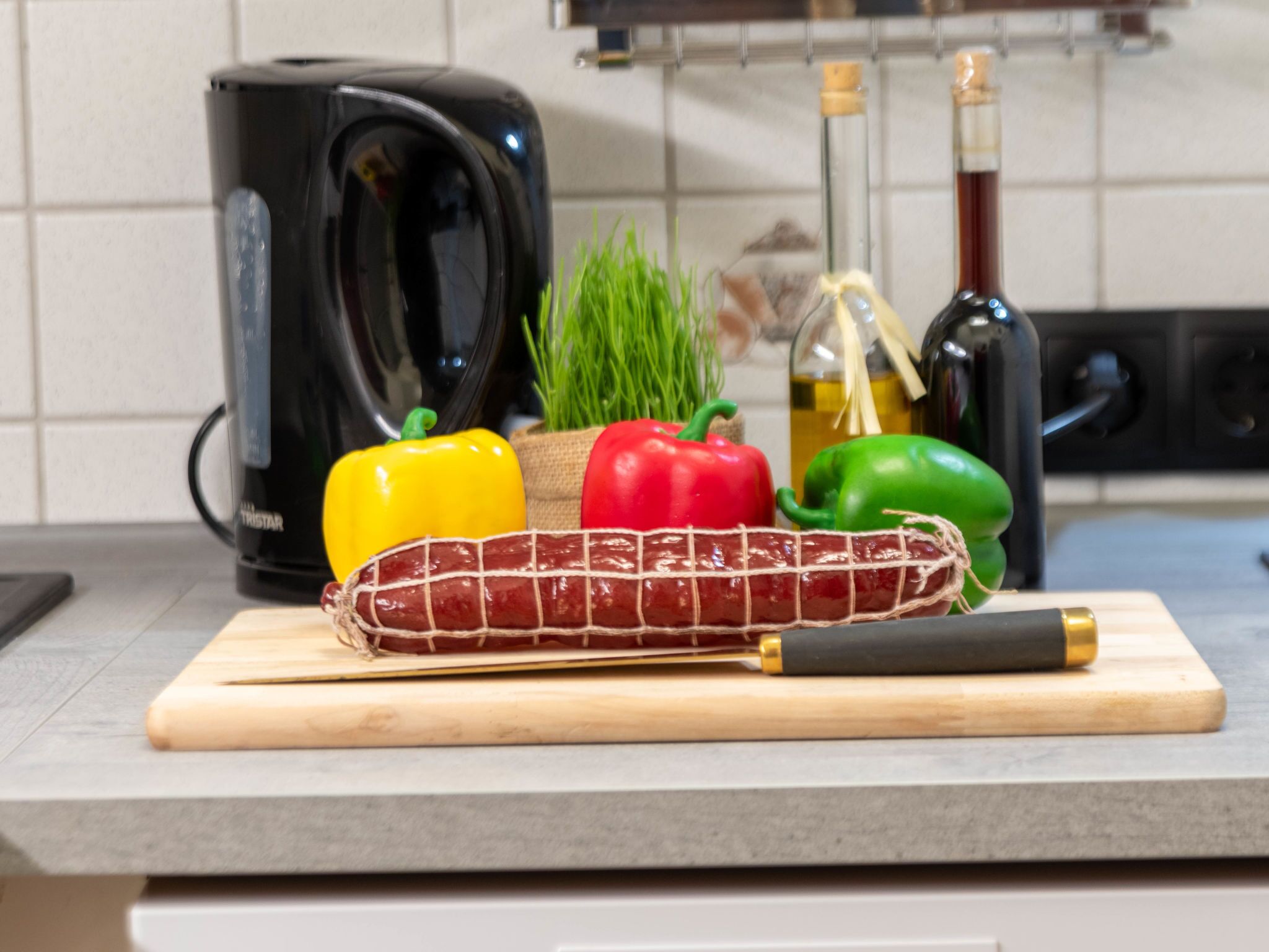 Eine Küchenarbeitsplatte mit Schneidebrett, einer Wurst und bunten Paprikaschoten.