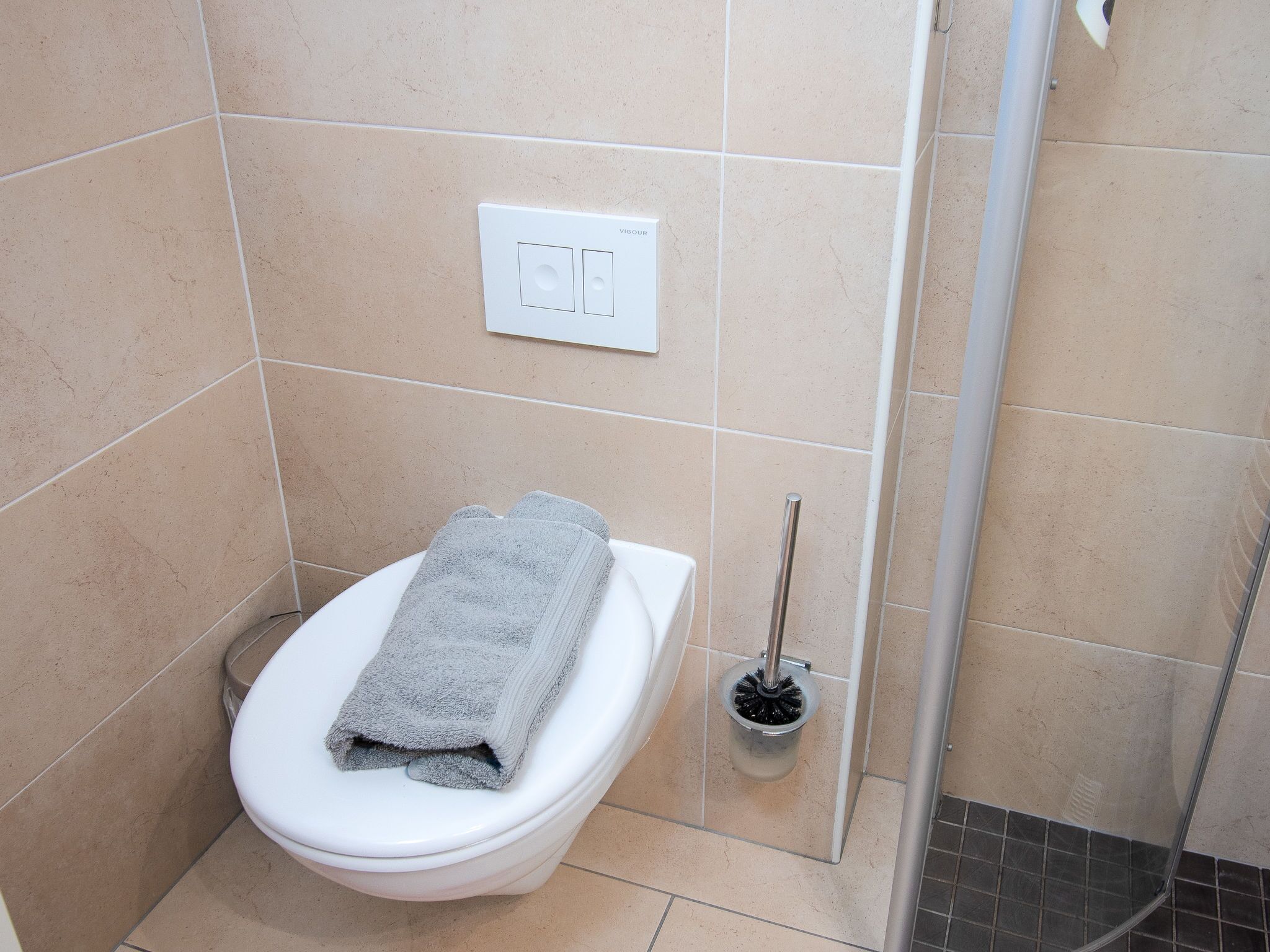 Une salle de bain équipée de toilettes, d’un sèche-mains et d’une brosse pour les toilettes.