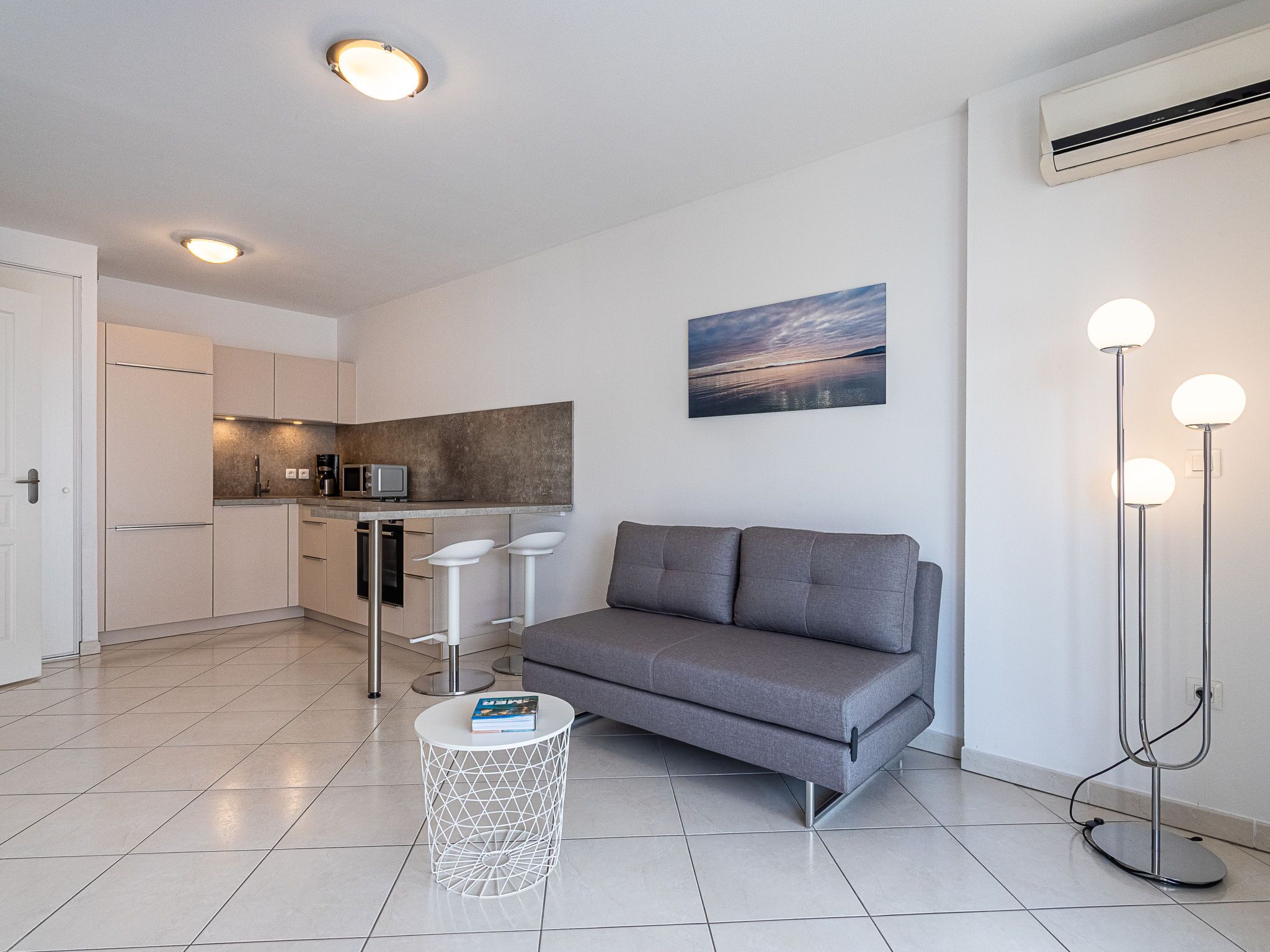 A modern living space with a grey sofa, a small round table, and a kitchen area.