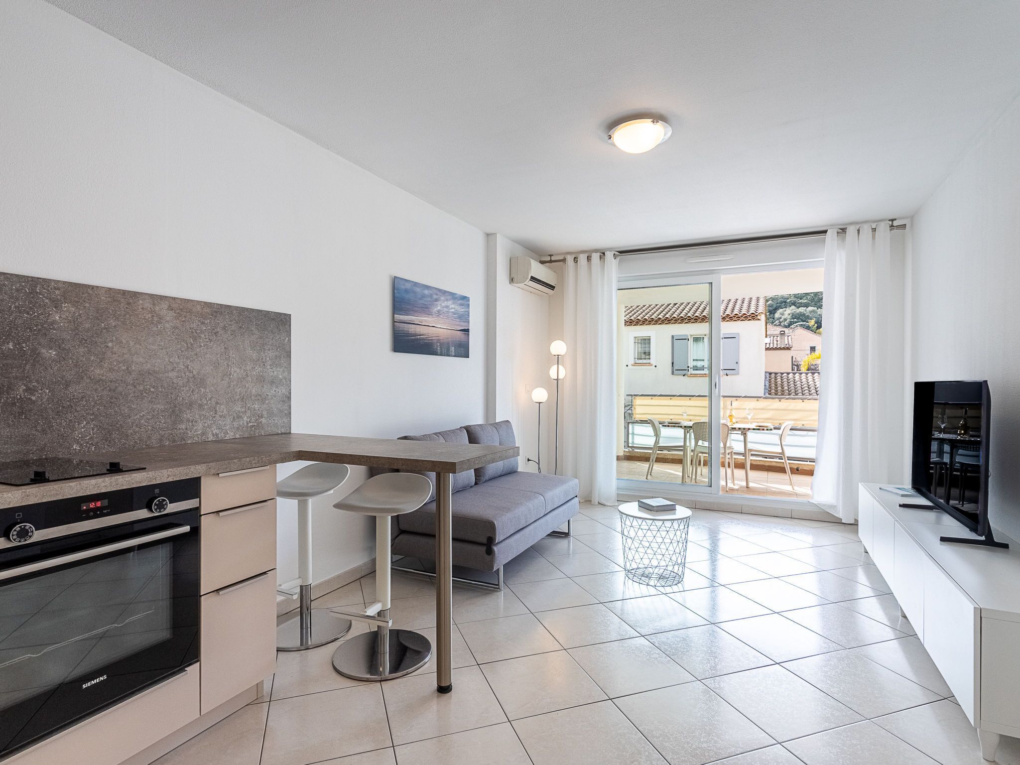 Una cocina moderna con horno Siemens, un sofá gris y una zona de comedor con mesa y sillas.