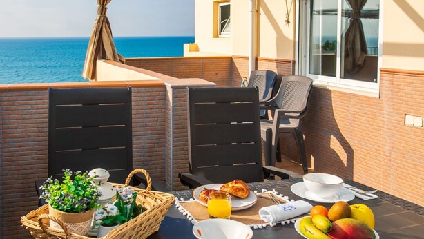Un balcon avec une table préparée pour le petit-déjeuner, comprenant des fruits, du pain et une boisson, et offrant une vue sur la mer.