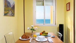 Un coin repas avec une table mise pour le petit-déjeuner, un tableau accroché au mur et une fenêtre donnant sur la mer.