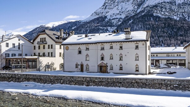 Un edificio cubierto de nieve con un muro de piedra al frente, con montañas al fondo.