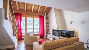 Una sala de estar moderna con techo de madera, un sofá, un televisor y un balcón con cortinas rojas.