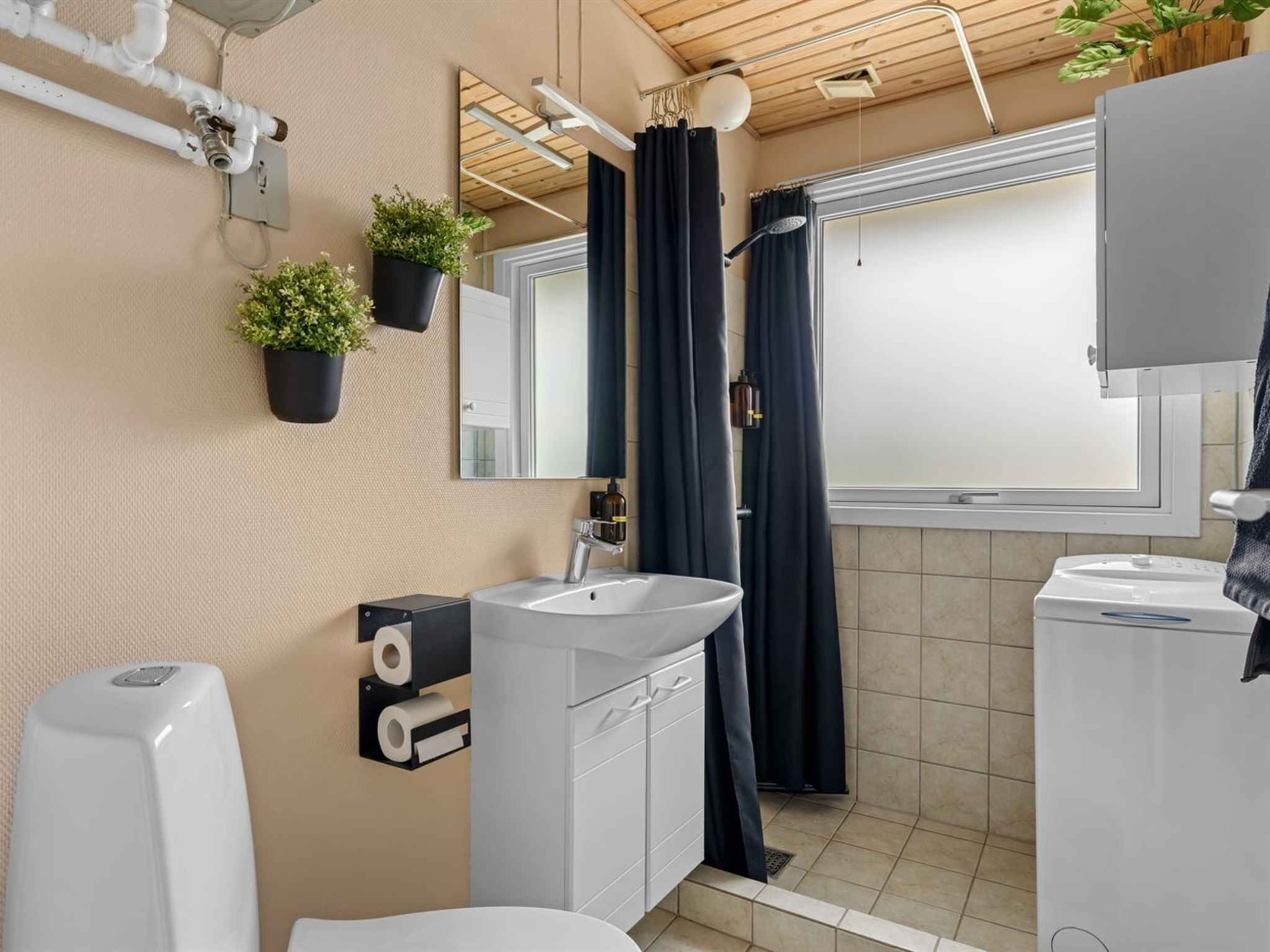 A modern bathroom with a toilet, sink, and shower. There are plants on the wall, a mirror, and a window.