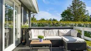 A covered outdoor seating area with a sofa and a table, surrounded by a wooden deck and a white railing. - "Bjart" - 150m from the sea by Interhome (Hesselager)
