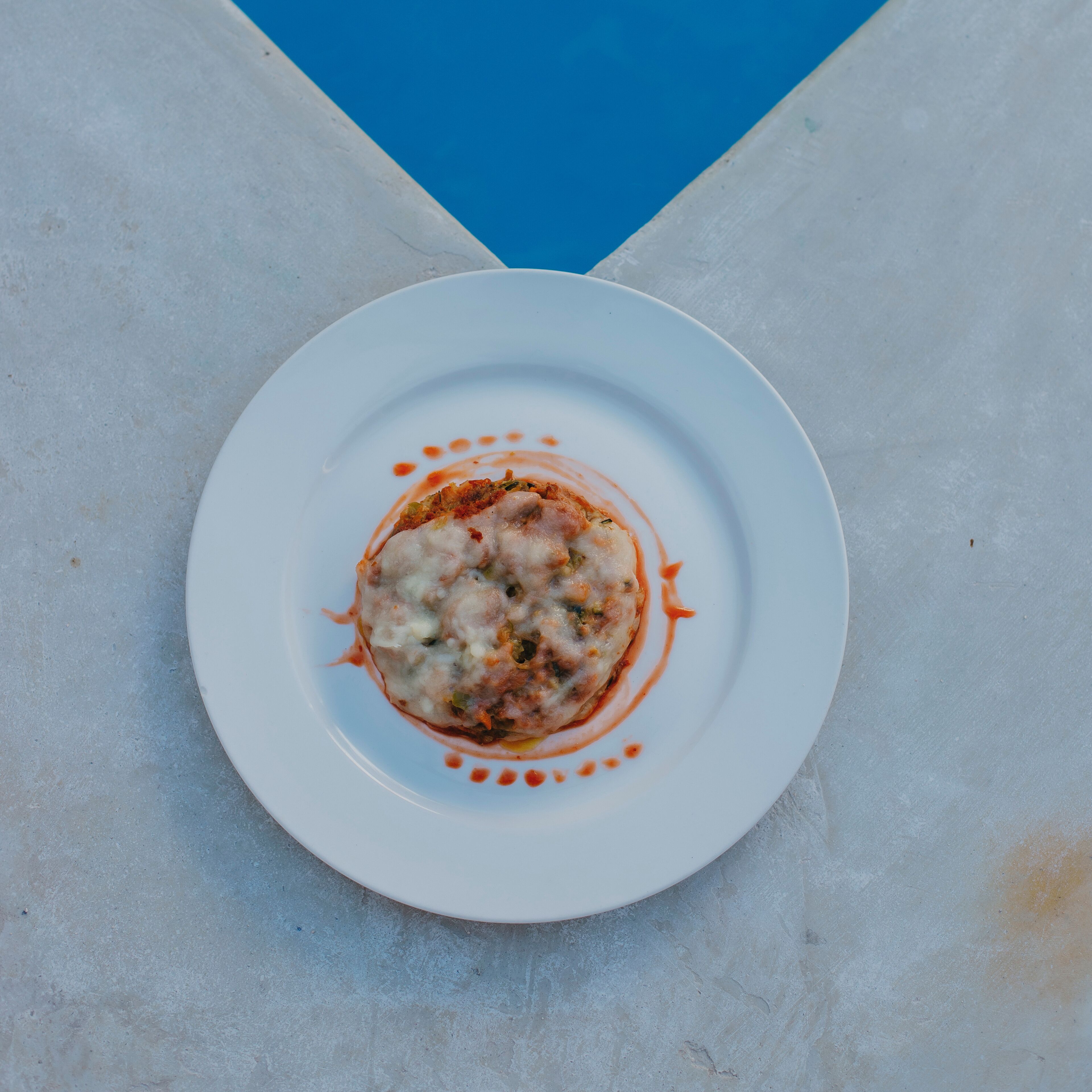 A white plate with a food item and sauce on a concrete surface.