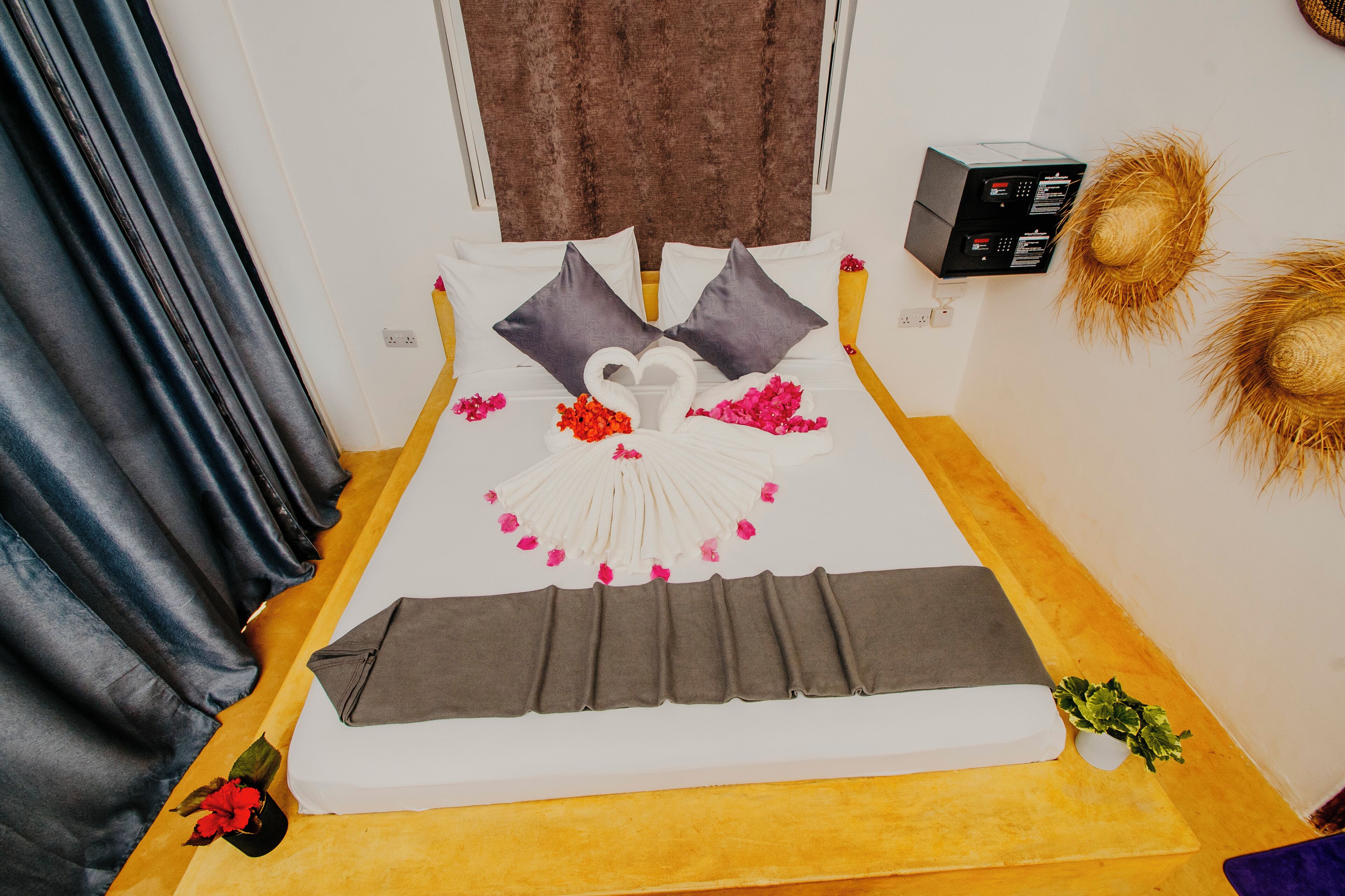 A neatly made bed with a swan-shaped pillow arrangement, a small plant, and decorative elements like a hat and a box on the wall.