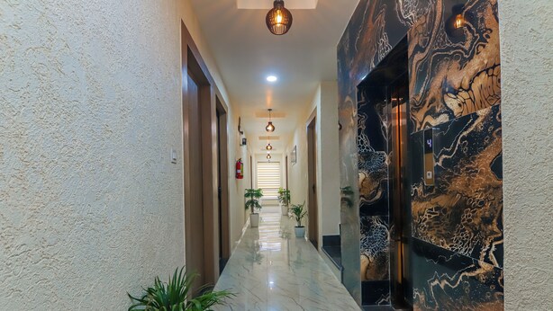 Un couloir d’hôtel avec un sol en marbre, des plantes en pot et un mur orné d’un motif évoquant le marbre.