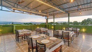 Un espace de restauration en plein air, avec des tables et des chaises, offrant une vue sur le paysage et doté d’une structure de toit abritée.