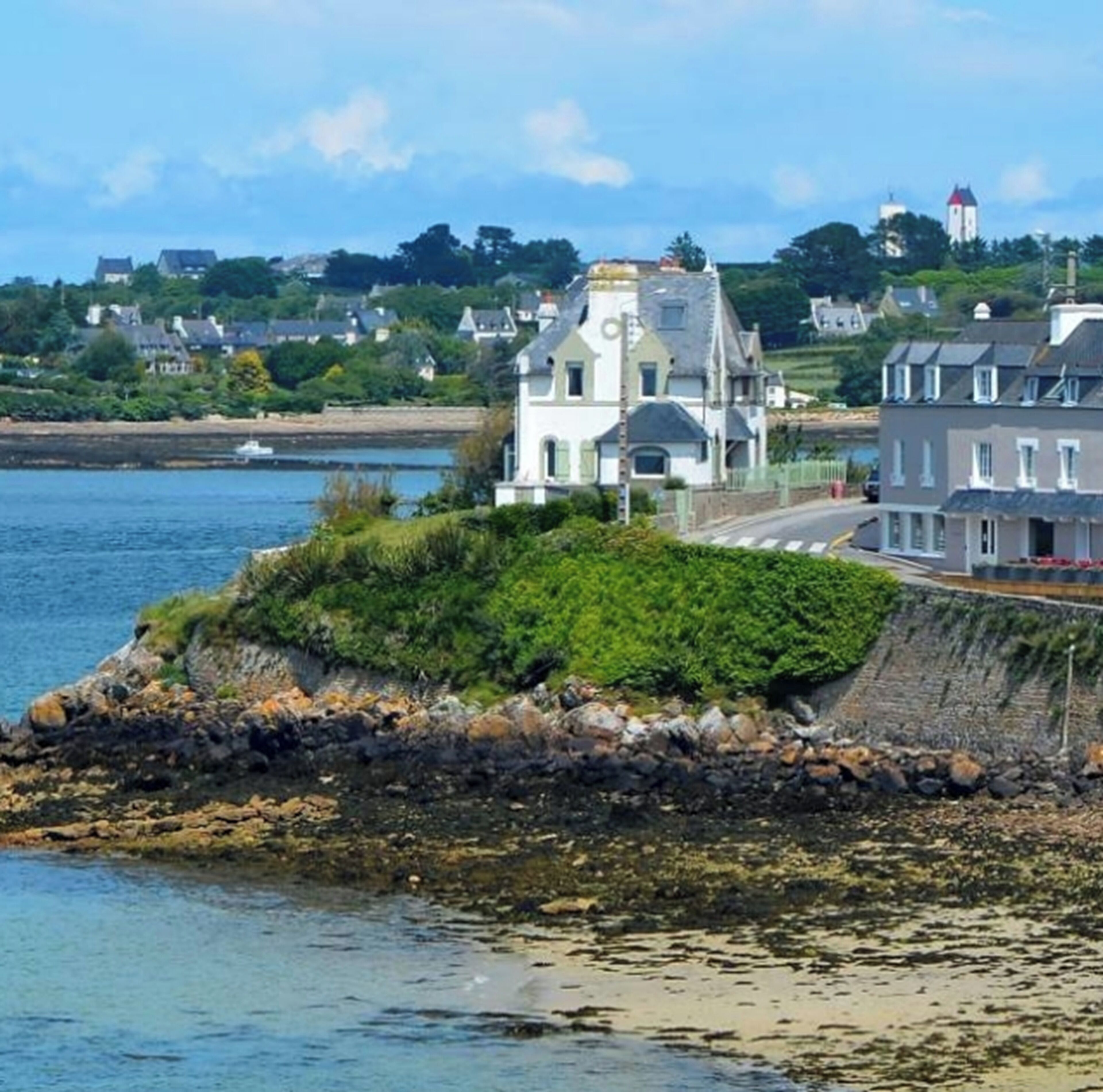 A coastal town with a prominent white building with a clock tower, situated near a body of water.