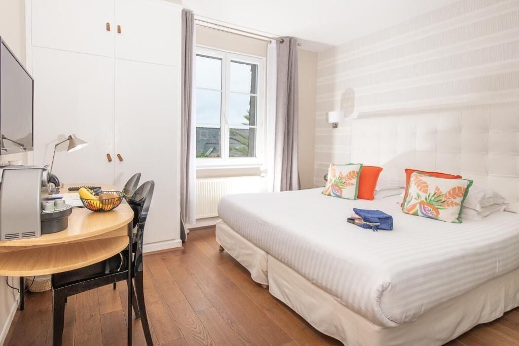 Een hotelkamer met een bed, een bureau met een computer, een stoel en een raam met gordijnen.