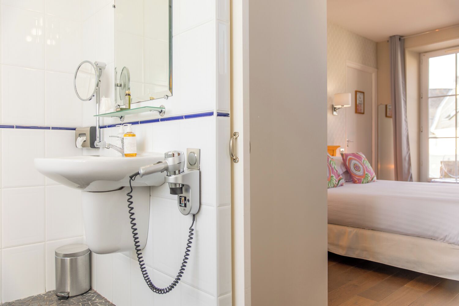 Un baño con lavamanos, espejo y secador de pelo, y un dormitorio con cama y ventana.