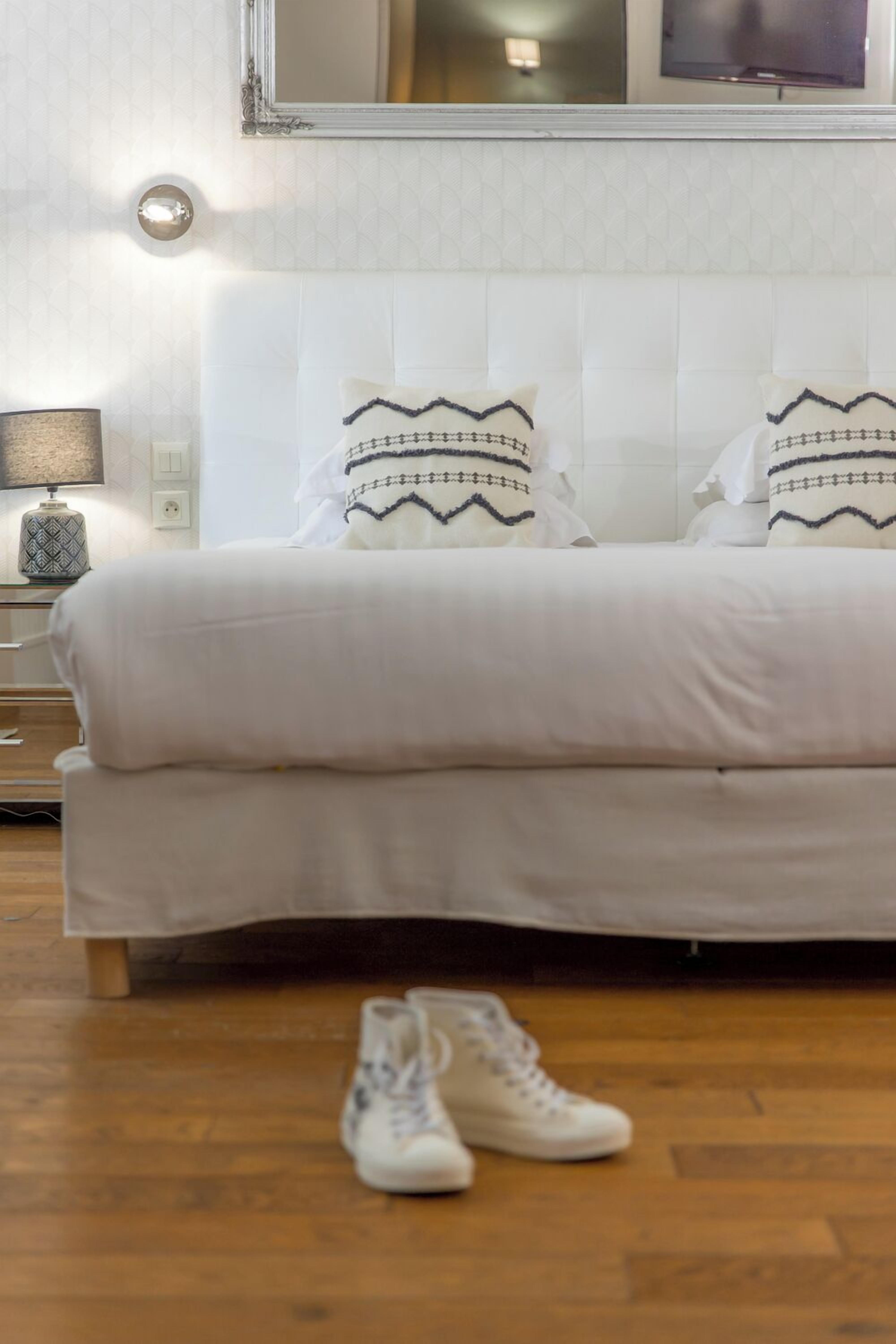 A neatly made bed with patterned pillows, a bedside lamp, and a pair of shoes on the floor.