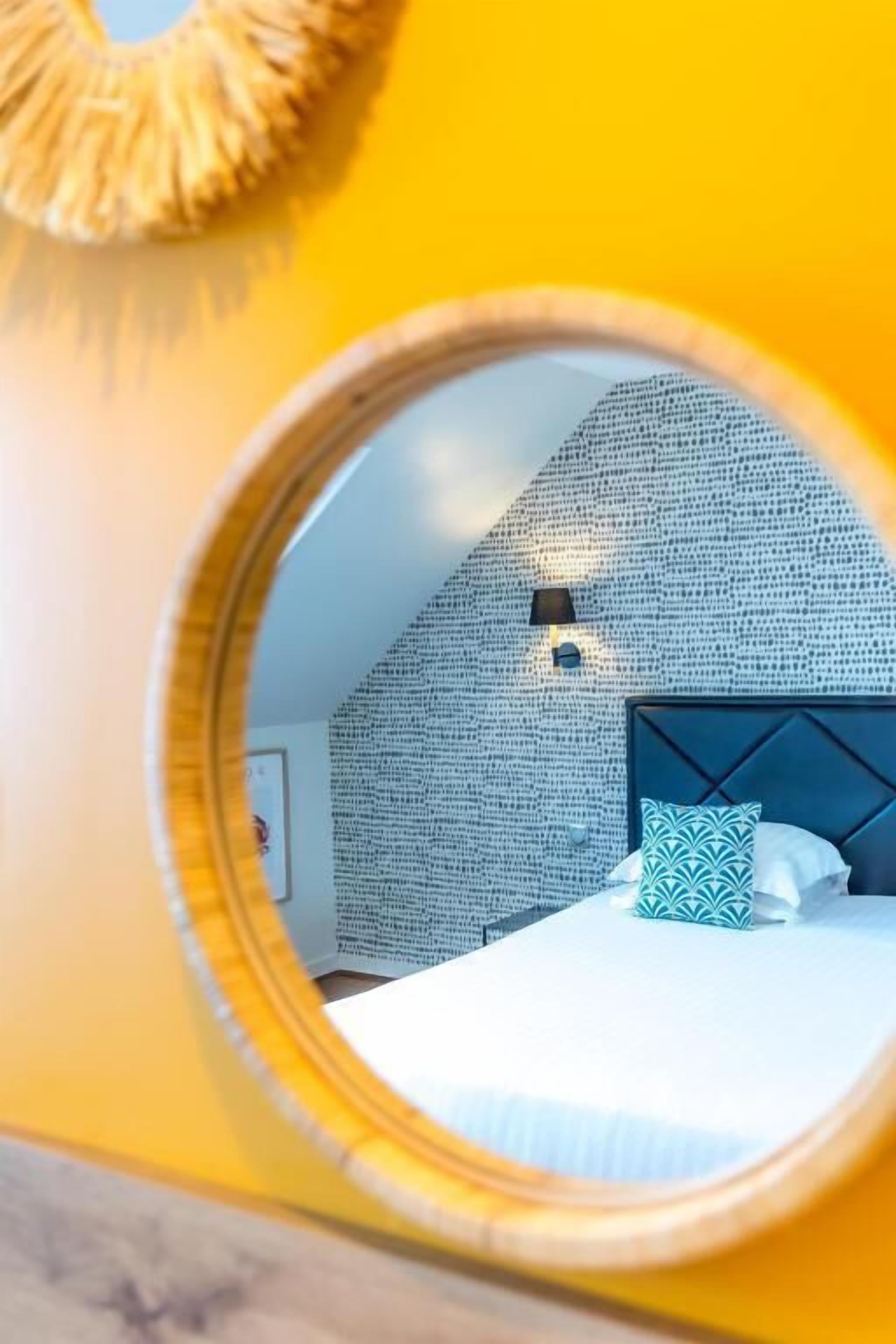 Ein runder Spiegel spiegelt ein Schlafzimmer mit einer Wand mit Muster, ein Bett mit Kissen und eine Wandleuchte.