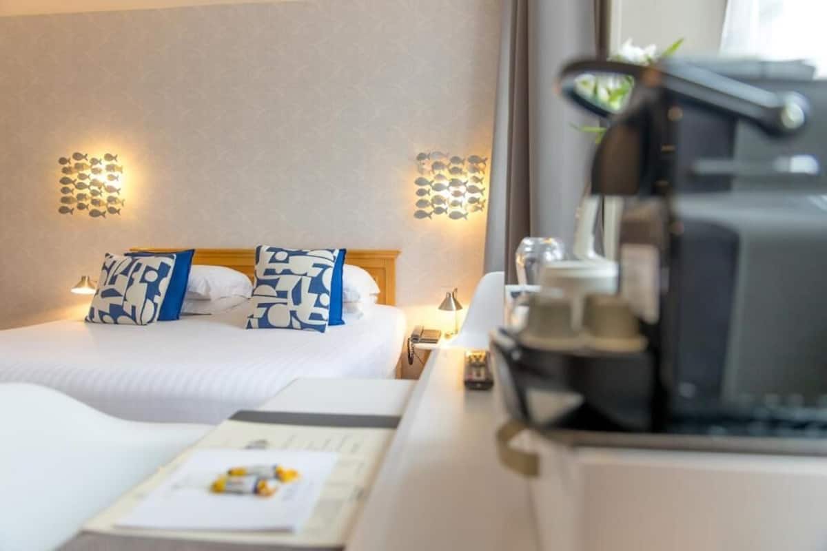 A hotel room with a bed, pillows, a desk with a lamp, and a coffee machine.