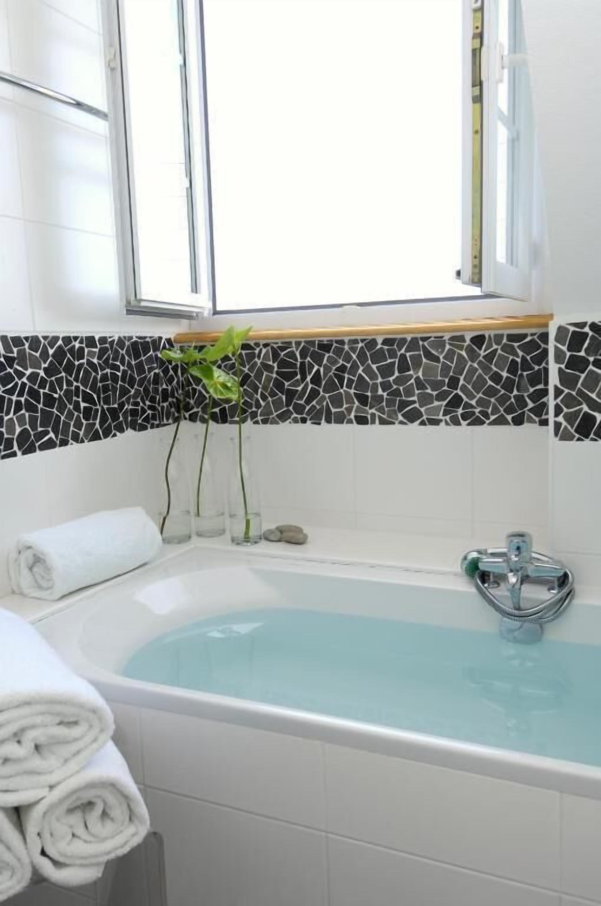 Un baño moderno con bañera, ventana y un salpicadero de mosaicos.