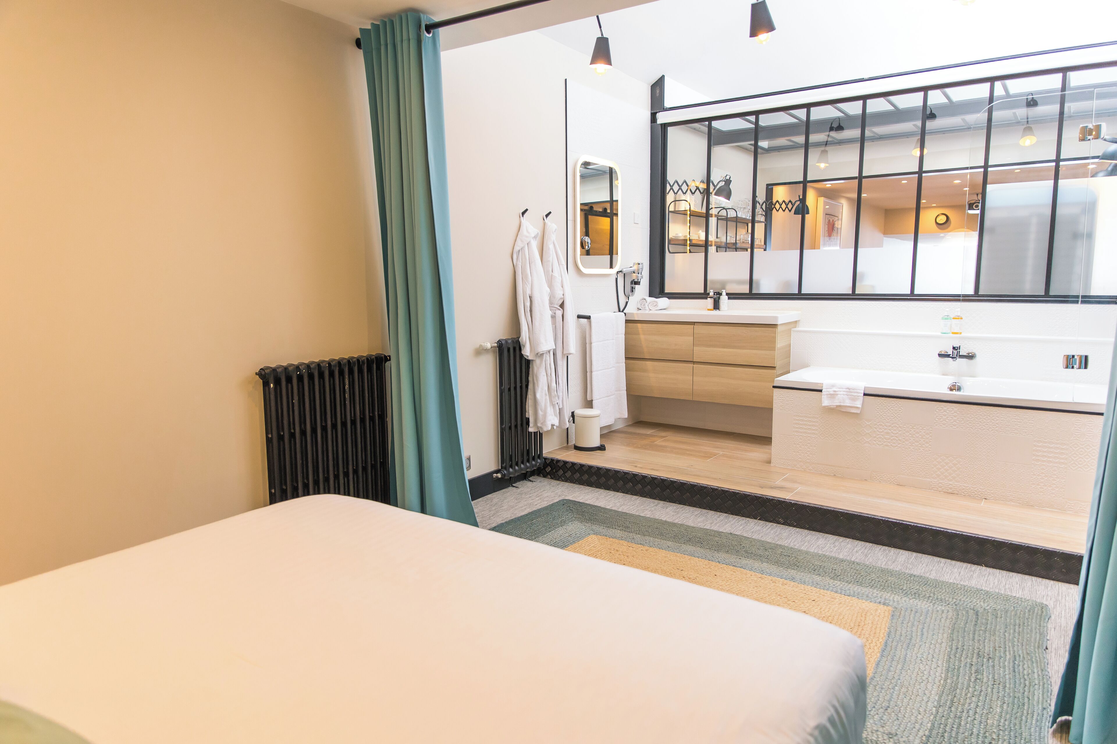 Une chambre d’hôtel moderne, équipée d’un lit, d’une salle de bain avec baignoire, d’une fenêtre donnant sur la cour et d’un radiateur.