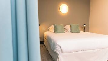 A neatly made bed with white and green pillows in a hotel room with a wall-mounted light fixture.