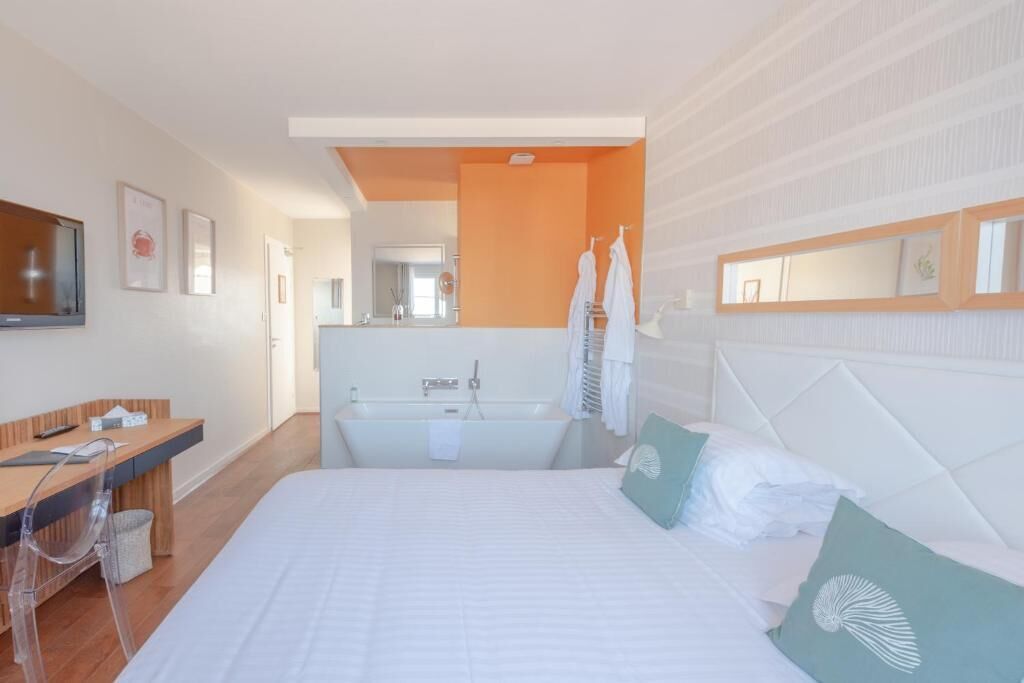 A modern hotel room with a large bed, a desk, a bathtub, and a mirror.