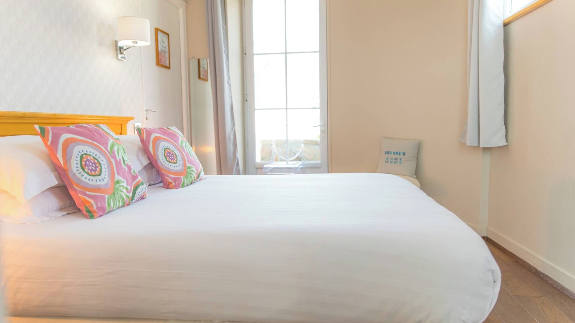 A hotel room with a large bed, a nightstand, a wall-mounted lamp, and a window with curtains.
