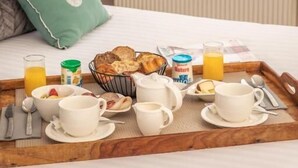 A breakfast tray with various items on a bed near a window overlooking a body of water. - Hôtel la Baie des Anges, son SPA marin et sa piscine couverte et chauffée (Landéda)