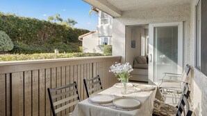A balcony with a table set for dining, chairs, and a vase with flowers. - Pool + Hot Tub Access + Gym | Gated, Newport Beach | Seabreeze Retreat (Dana Point)