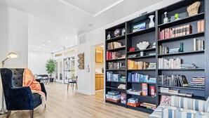 A spacious living area with a dark blue sofa, a striped armchair, and a black bookshelf filled with books and decorative items. - Pool + Hot Tub Access + Gym | Gated, Newport Beach | Seabreeze Retreat (Dana Point)