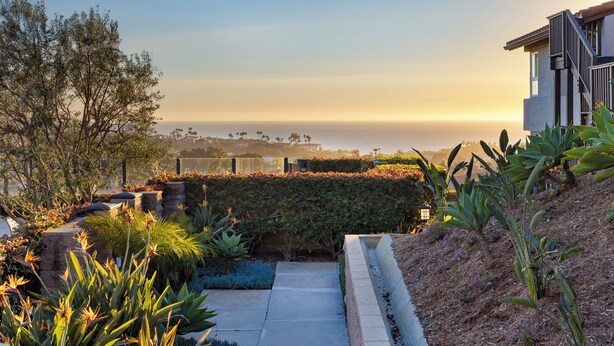 A landscaped garden with a pathway leading to a building with a view of the ocean. - Pool + Hot Tub Access + Gym | Gated, Newport Beach | Seabreeze Retreat (Dana Point)