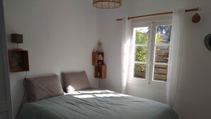 A bedroom with a bed, a bedside table, a lamp, a window with curtains, and a view of greenery outside.