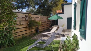 A backyard with a wooden deck, a green umbrella, and a white wall with green shutters.