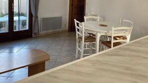 Un espace repas avec une table et des chaises blanches, un banc en bois et un luminaire suspendu au plafond.