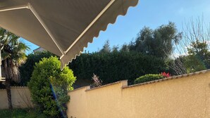 Un espace patio avec une table et des chaises blanches, un sol carrelé et un coin salon abrité.