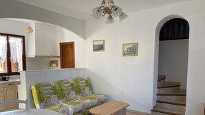 Un espace de vie compact comprenant un canapé, une table à manger, un banc, un coin cuisine et un escalier menant à un niveau supérieur.