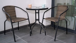 Deux chaises en osier avec des armatures métalliques, une petite table ronde et deux tasses posées sur la table.