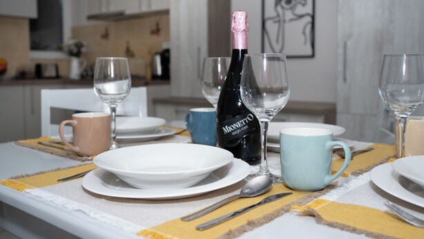 Une table à manger dressée avec des assiettes, des couverts, des verres et une bouteille de vin Mionetto.