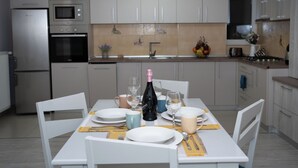 Une cuisine moderne avec des armoires blanches, un four encastré et un four à micro-ondes. On y trouve une table à manger mise avec des assiettes, des verres et une bouteille de champagne.