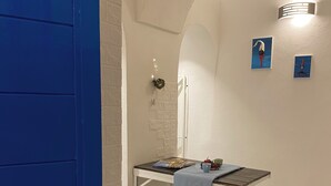 Une pièce avec une porte bleue, un mur blanc orné d’un motif en briques, une petite table recouverte d’une nappe bleue et deux tableaux encadrés.